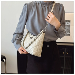 Détail du sac matelassé crème avec chaîne argentée porté par un mannequin