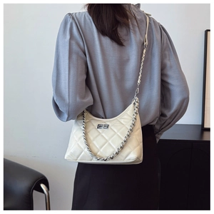 Détail du sac à chaîne matelassé beige porté à l'épaule montrant la texture élégante