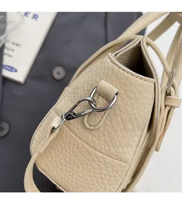 Detail shot of silver metal hardware and fine stitching on beige lychee leather bag