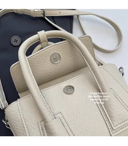 Detail of beige lychee grain leather texture and magnetic snap closure on handbag