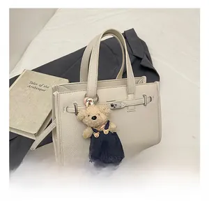 Detail of cream leather handbag with lychee grain texture and cute teddy bear charm