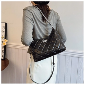 Détail d'un sac hobo matelassé noir avec chaîne argentée porté en bandoulière par un mannequin