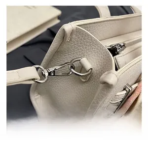 Detail of silver hardware D-ring and lobster clasp on cream leather crossbody bag
