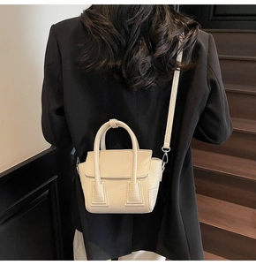 Rear view of off-white lychee pattern leather handbag worn over a black blazer jacket