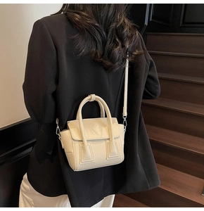 Detail shot of beige pebble grain leather handbag with silver hardware and top handle