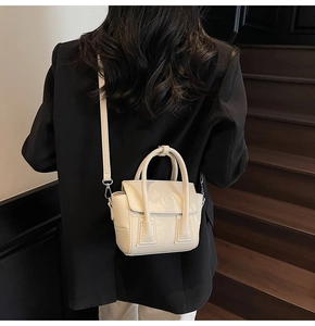 Detail view of a cream-colored leather mini crossbody bag with litchi grain texture