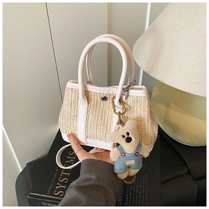 Detail of woven straw bucket bag with white leather trim and a cute plush bear charm