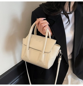Close-up of off-white lychee grain leather crossbody bag worn by model in black suit