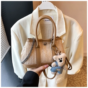 Detail of woven straw bag with leather trim and cute bear plush charm on white blazer