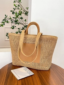 Large straw tote bag with brown leather pocket and handles on a wooden table