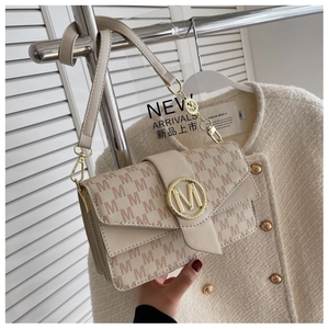Détail du sac beige avec tissu texturé à motif M et boucle métallique dorée élégante