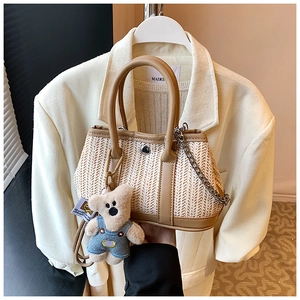 Detail of woven straw handbag featuring leather trim and a cute plush bear charm