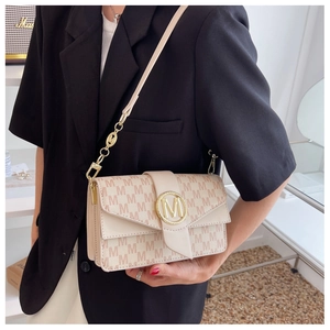 Sac bandoulière beige à motifs M et boucle dorée, porté avec un blazer noir chic