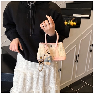 Close-up of woven straw handbag with pink leather handles and cute bear charm