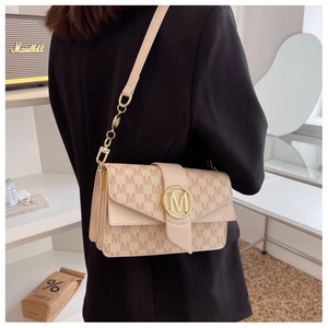 Détail du sac bandoulière beige avec motif M et boucle en métal porté par un mannequin