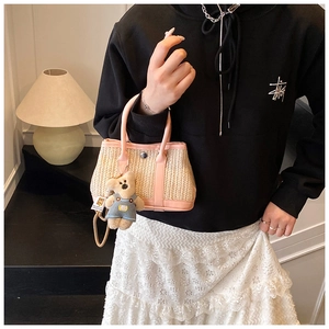 Detail of a woven straw handbag featuring pink leather trim and a cute teddy bear pendant