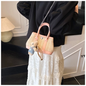 Pink woven straw beach bag with plush bear charm and chain strap shown on a model