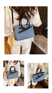Detail of light blue denim bucket bag featuring black leather handles and metal hardware