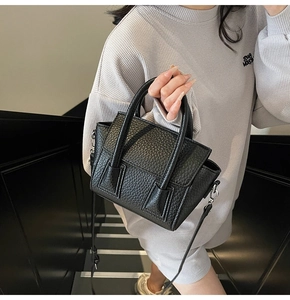 Detail of black pebbled leather mini tote bag held by model on dark stairs