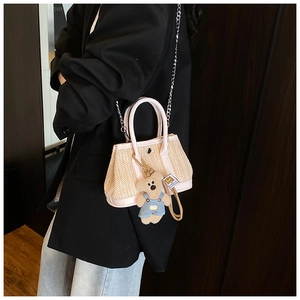 Detail of a straw handbag featuring pink leather trim and a cute blue teddy bear pendant