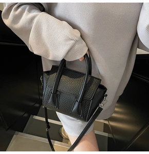 Close-up of black lychee grain texture and silver buckles on a small trapezoid bag