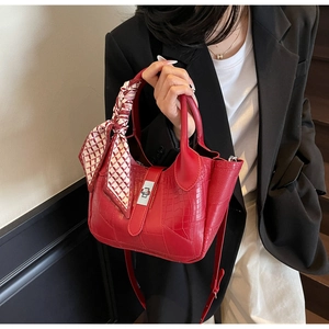 Detail of red croc-embossed bucket bag with decorative silk scarf on handle