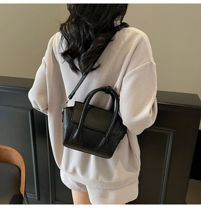 Model wearing a black pebble leather mini crossbody bag with a modern minimalist style