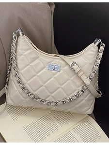 Sac bandoulière matelassé beige avec chaîne argentée posé sur un livre ancien