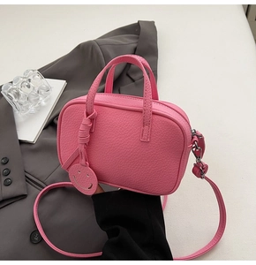 Macro view of bright pink pebbled leather crossbody bag with a cute smiley face charm