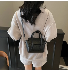 Detail of a black pebbled leather mini handbag styled on a model in a minimal interior