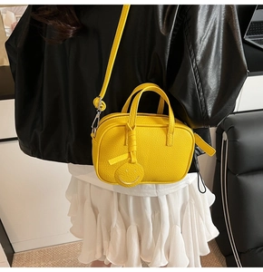 Detail of bright yellow lychee leather crossbody bag with cute smiley tag on a model