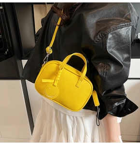 Close-up of bright yellow mini crossbody bag with smiley tag on a black leather jacket
