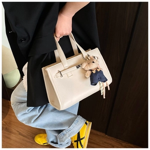 Detail of off-white lychee texture tote bag with a cute teddy bear charm accessory