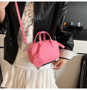 Detail of pink mini pillow bag with smiley charm on a model in leather jacket