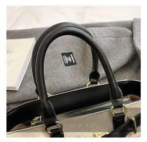 Close-up of elegant beige tote bag featuring black leather handles and gold hardware