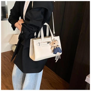 Chic cream-colored leather tote bag with a cute teddy bear charm on a female model