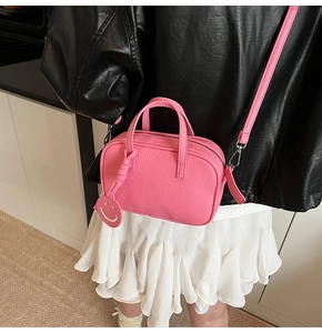 Detail of pink pebbled leather crossbody bag featuring a smiley face charm and silver zipper