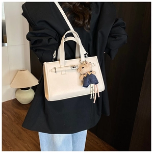 Detail of beige textured leather handbag with silver lock and cute bear charm