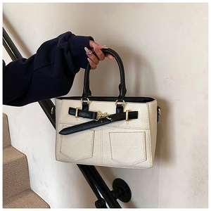 Detail of cream bucket bag with black handles and gold metal lock held by model
