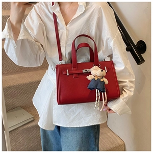 Detail of red lychee leather tote bag featuring a silver twist lock and cute bear charm