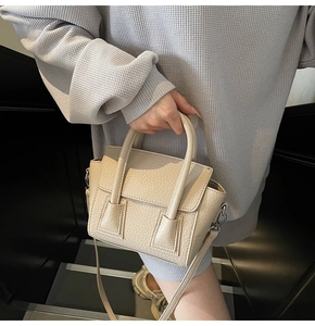 Detail of beige lychee pattern texture on a stylish handbag with crossbody strap