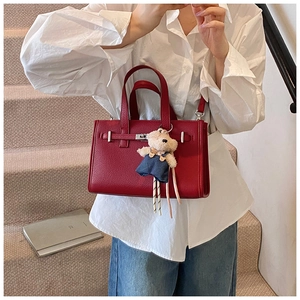 Detail of red lychee textured leather handbag with silver clasp and plush bear charm