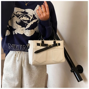 Close-up of cream bucket bag featuring black handles and leather strap with metal buckle