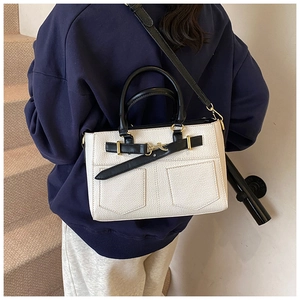 Model wearing a white pebbled leather bucket bag with black straps and gold metal clasp