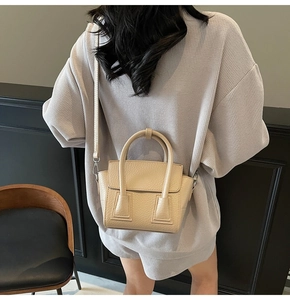 Rear view of a model carrying a beige lychee pattern leather handbag with silver hardware