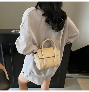 Detail of a beige trapezoid crossbody bag with litchi texture and dual top handles