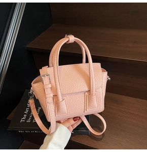 Pink mini leather handbag with lychee texture on dark wood stairs with books