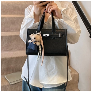 Detail of black pebbled leather handbag with silver twist-lock and cute bear charm