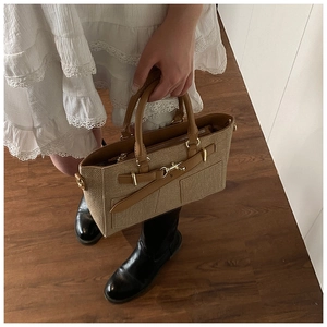 Detail of straw woven handbag with brown leather trim held by model in white dress