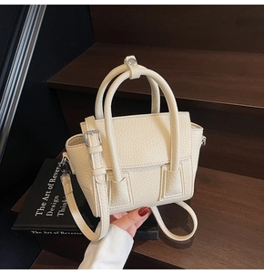 Detail of cream lychee texture leather handbag with circular handles and metal buckles